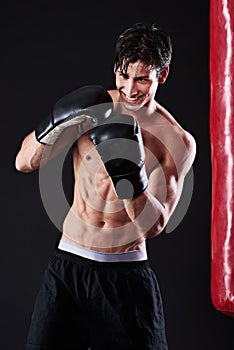 Man, boxing gloves and smile at bag for martial arts practice in studio for fitness, exercise or black background. Male