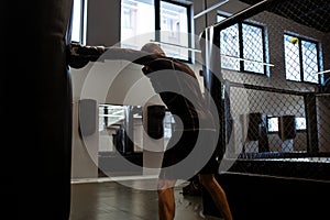 Man in boxing gloves training with heavy bag in gym