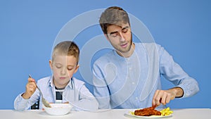 A man and a boy sit at the table, a man eats fast food, and a boy eats porridge. The concept of healthy and unhealthy