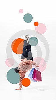 Man, breakdancer standing on one hand, clutching shopping bags filled with Black Friday deals against white background photo