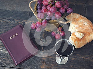 Man breaking the bread, with wine, grapes and Bible in the background