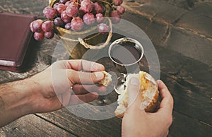 Man breaking the bread, with wine, grapes and Bible in the background