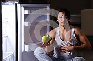 The man breaking diet at night near fridge