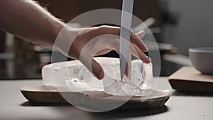 man breaking ice block with knife on olive wood board