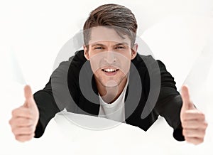 Man breaking through paper wall and showing thumbs up