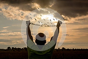 A man breaks the chain that crumbles into birds against the backdrop of a sunny sunset