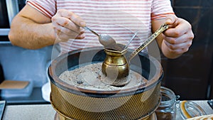 A man brews a Turkish coffee on the sand in the pot, hands close up. Coffee made on the sand in ibrik or ibriq. Coffee photo