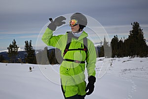 Man in bright acid green snowboard suit, black warm gloves, orange ski goggles, black helmet and backpack. skier outfit photo