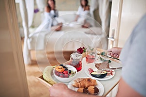 Young man bringing breakfast in bed for two female. lesbian, bisexual, threesome concept