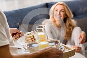 Man bringing tray with tasty breakfast to happy blonde woman