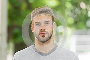Man with bristle on calm face, nature background, defocused. Man with beard or unshaven guy looks handsome outdoor. Guy