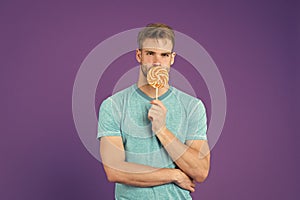 Man with bristle likes lollipop. Cheat meal concept. Sugar harmful for health. Guy hold lollipop candy violet background