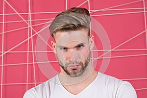 Man with bristle on strict concentrated face, pink background. Guy bearded and attractive with hairstyle. Masculinity