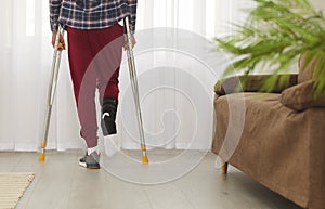 Man with broken leg, foot or ankle using crutches and standing by window at home