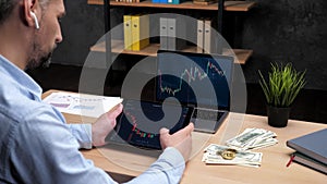 Man broker scrolling tablet with stock exchange chart, laptop with stock market