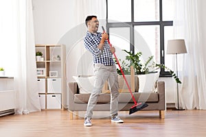 Man with broom cleaning and singing at home