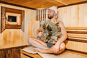 A man with a broom in his hand is relaxing in the sauna