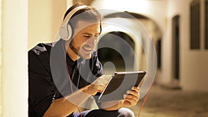 Man browsing on tablet wearing headphones in the night