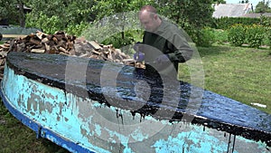 Man brush with resin an old boat bottom in garden outdoor. 4K