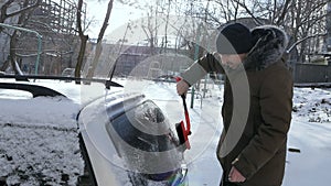 A man brushes a car windshield from snow. In winter, the car was covered with snow