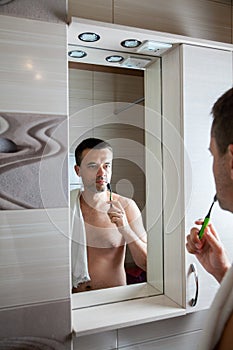 Man brushes his teeth in front of mirror in the bathroom at home in morning
