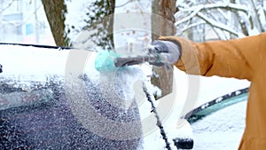 A man brushes snow from a car after a snowfall. A hand in a mustard jacket with a car broom on the white body. Winter weather cond