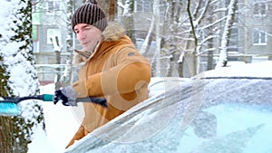 A man brushes snow from a car after a snowfall. A hand in a mustard jacket with a car broom on the white body. Winter weather cond