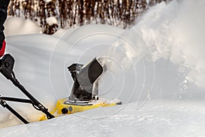 Man is brushing white snow with the yellow electric snow thrower in a winter garden