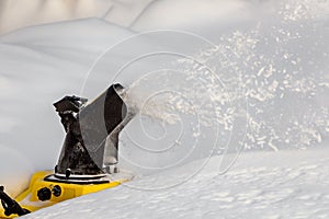 Man is brushing white snow with the yellow electric snow thrower in a winter garden