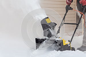 Man is brushing white snow with the yellow electric snow thrower in a winter garden