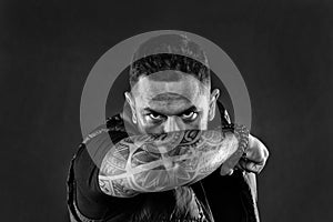 Man brutal guy cover face with tattooed arm. Tattooed elbow hide male face dark background. Visual culture concept