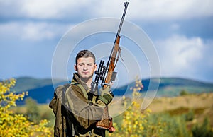 Man brutal guy gamekeeper nature background. Hunter rifle gun stand top of mountain. Guy bearded hunter spend leisure