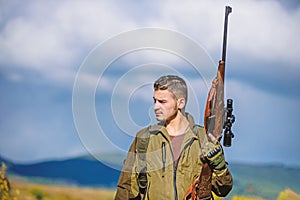 Man brutal guy gamekeeper nature background. Regulation of hunting. Hunter rifle gun stand top of mountain. Guy bearded