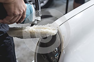 A man buffing the circular headlights of a sedan with a wool pad attached to a rotary. masking tape placed on edges for protection