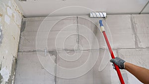 A man builder priming a wall before doing further work with a construction roller. Priming the wall with a roller