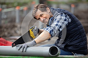 man builder sawing pipe with hand modern saw
