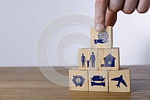 Man building pyramid of cubes with different icons on wooden table against light background, closeup. Insurance concept