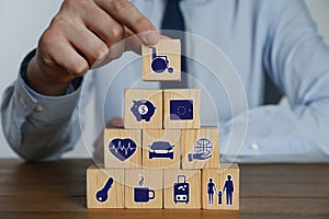 Man building pyramid of cubes with different icons at wooden table, closeup. Insurance concept