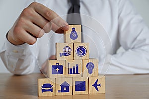 Man building pyramid of cubes with different icons at wooden table, closeup. Insurance concept