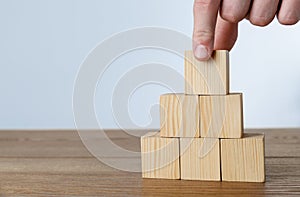 Man building pyramid of cubes on wooden table against light background, closeup. Space for text