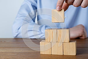 Man building pyramid of cubes on wooden table, closeup. Space for text