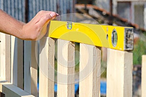 Man building a wooden fence and checking with spirit level. Close up of his hand and the tool in a DIY concept.