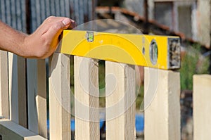 Man building a wooden fence and checking with spirit level. Close up of his hand and tool.