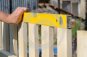 Man building a wooden fence and checking with spirit level. Close up of his hand and the tool in a DIY concept.