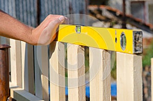 Man building a wooden fence and checking with spirit level. Close up of his hand and the tool in a DIY concept.