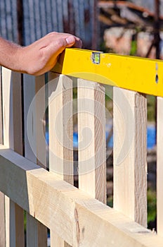 Man building a wooden fence and checking with spirit level. Close up of his hand and the tool in a DIY concept.