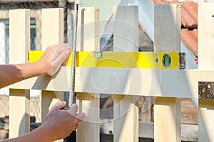 Man building a wooden fence and checking with spirit level. Close up of his hand and the tool in a DIY concept.