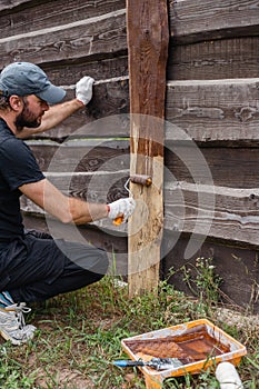 A man builds and paints a fence from rough boards