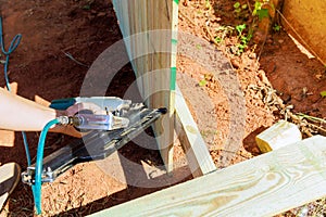 Man builds sections of a wooden fence around his yard using an air nail gun to attach planks to it