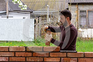 A man builds a wall of bricks, lays a brick on a cement-sand mortar.